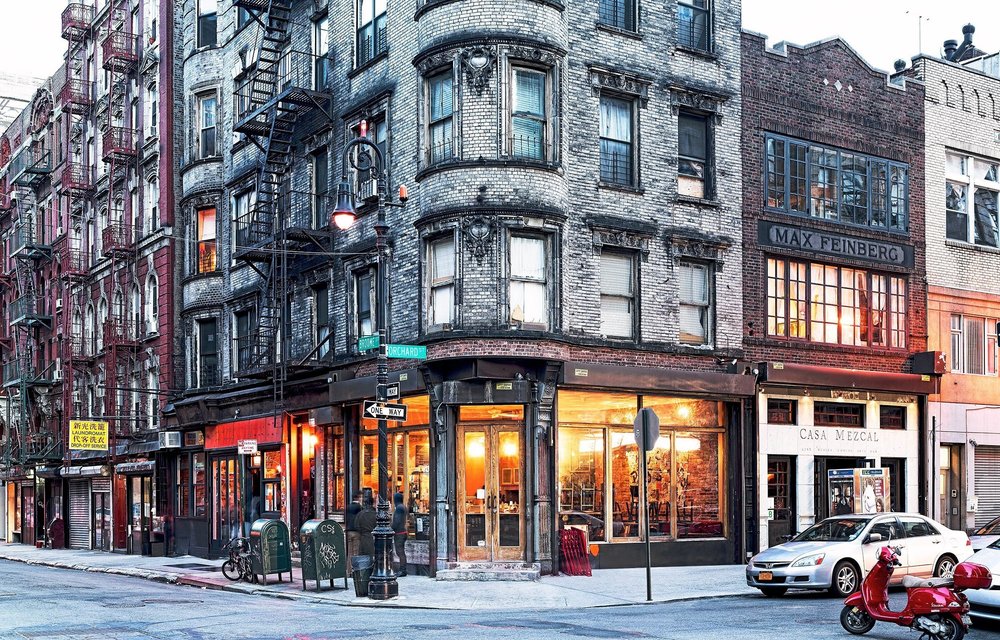 Orchard Street on the Lower East Side, with brick buildings, fire escapes and warmly lit storefronts